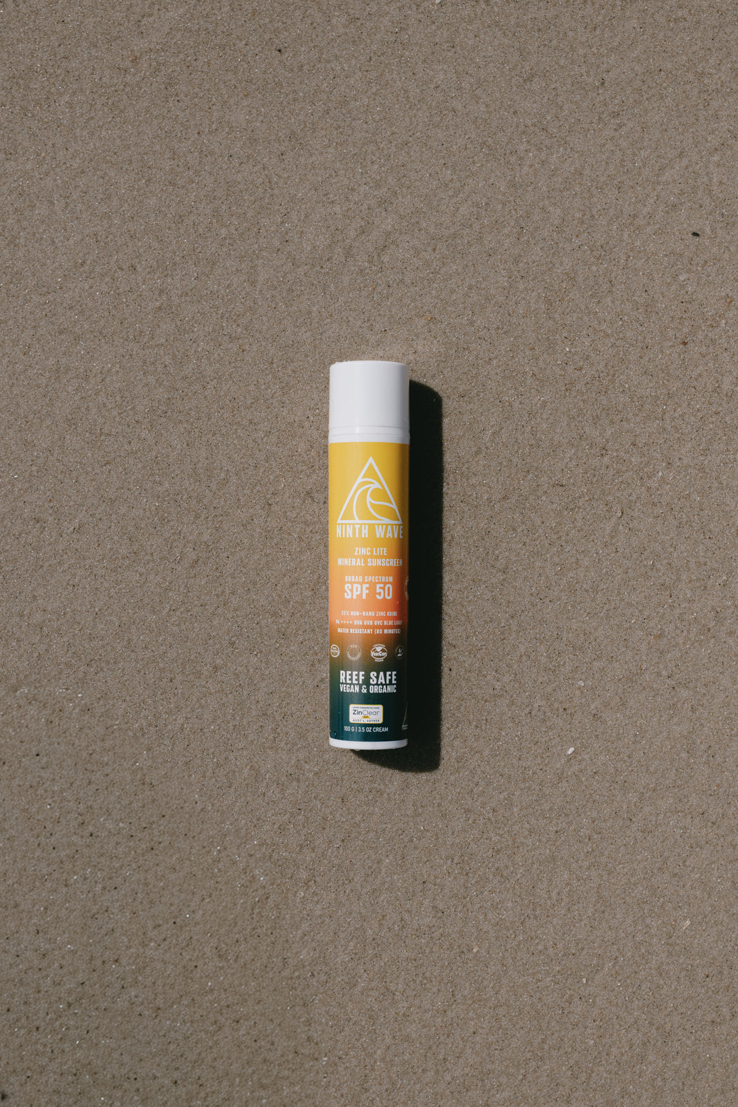 Ninth Wave Zinc Lite tube placed on the sand at the beach to highlight sun protection for surfers and outdoor days.