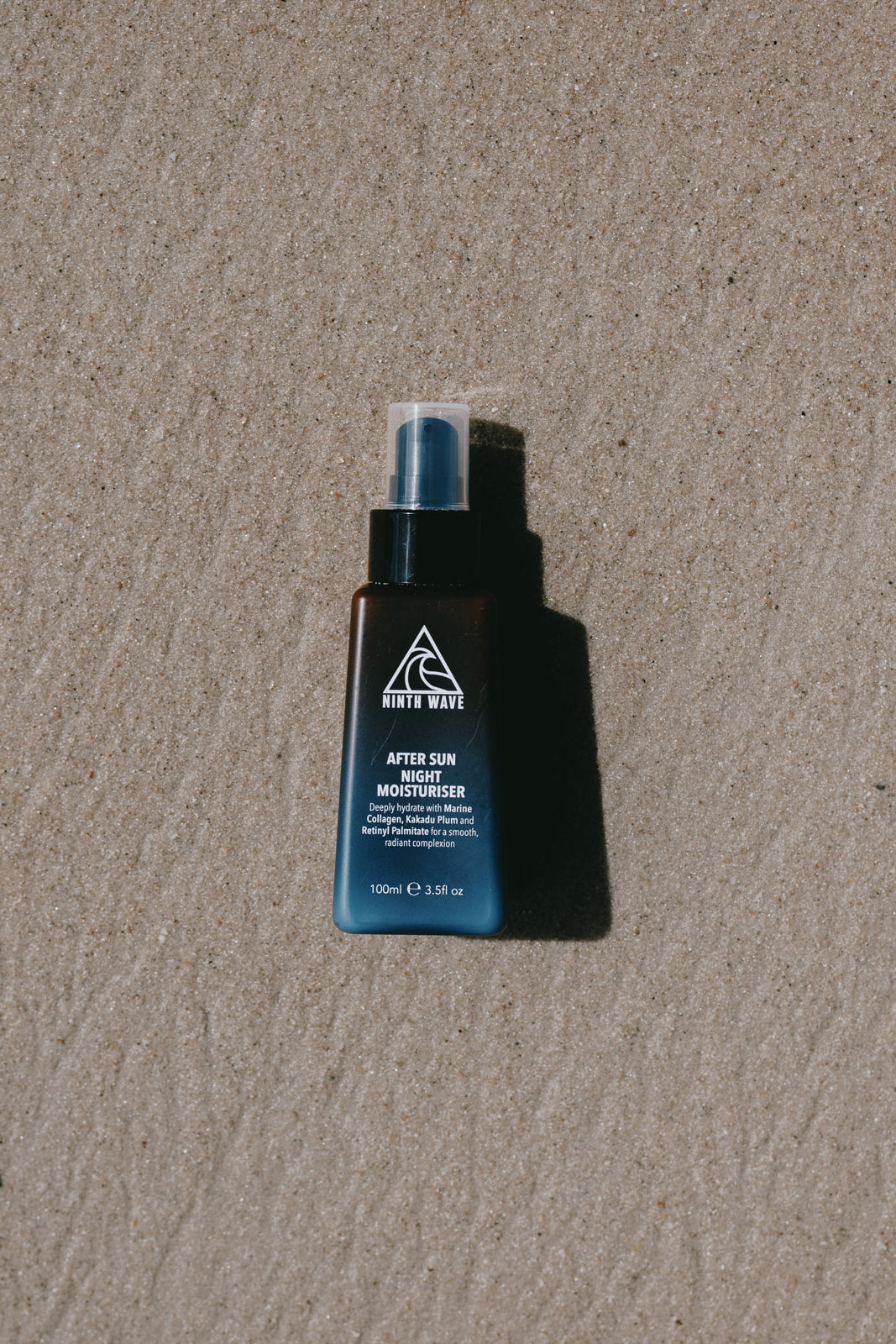 Ninth Wave After Sun Night Moisturiser bottle placed on the sand at the beach to highlight post-sun recovery