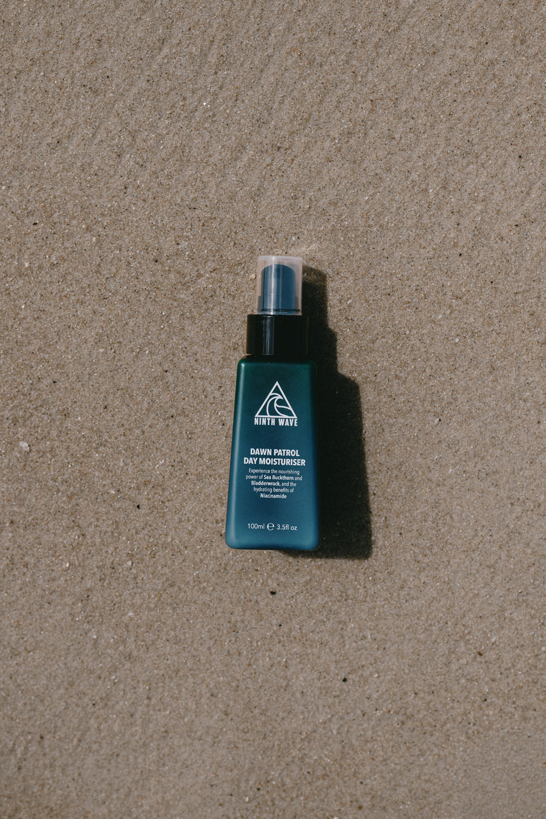 Ninth Wave Dawn Patrol Day Moisturiser bottle placed on the sand at the beach to reflect a surf-ready morning routine