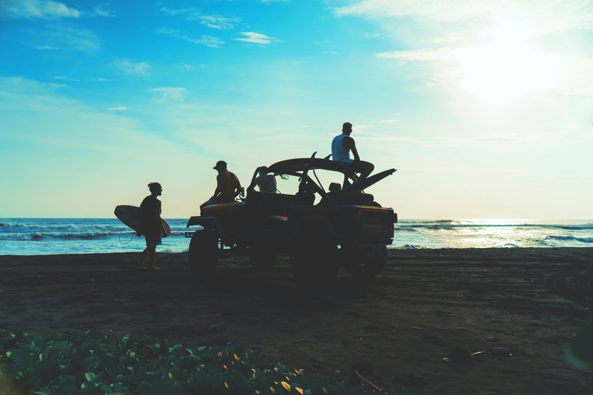 People on a beach with an off-road vehicle against a blue sky. 